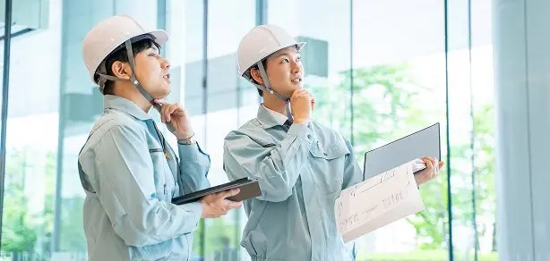 ヘルメットを着用した2名の社員が図面を持ちながら現場を確認している様子