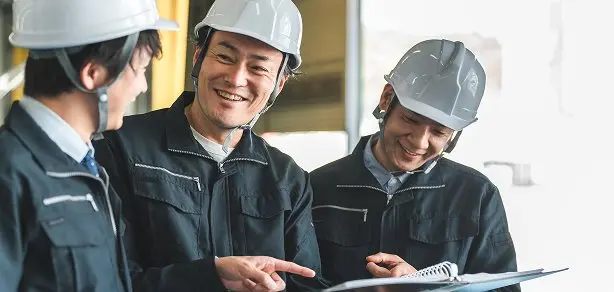 ヘルメット着用の3名の社員がタブレットを囲んで笑顔で話し合っている様子