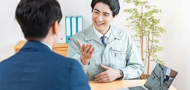 作業服の男性社員が対面で笑顔で打ち合わせをしている様子