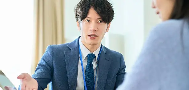 スーツ姿の男性社員が身振りを交えて説明している場面